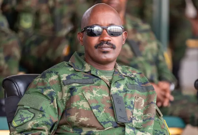 Brigadiye Jenerali Pascal Muhizi yicaye ku ntebe yambaye imyenda ya gisirikare n'indorerwamo. 