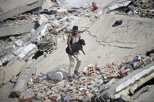 Un hombre lleva a un perro negro rescatado entre los escombros de un edificio derrumbado tras dos terremotos en Caraballeda, estado de La Guaira, a unos 40 km al noreste de Caracas, el 25 de junio de 2026.