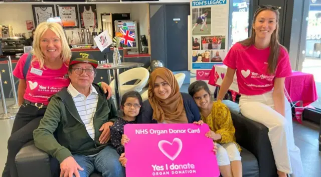 من اليسار إلى اليمين، ليزا ويلسون مع المتلقي غوردون، والمتلقية فاطمة ووالدتها لبنى وشقيقتها صوفيا، ثم ابنة ليزا (بيبا). يجلسون على أريكة، مبتسمين للكاميرا. تحمل الأم وابنتاها بطاقة وردية للتبرع بالأعضاء من هيئة الخدمات الصحية الوطنية، يتوسطها قلب ورسالة "نعم، أتبرع" باللغة الإنجليزية. تُعرض خلفهم منتجات متنوعة من ألعاب التنافس لزراعة الأعضاء، بالإضافة إلى معلومات عن ابن ليزا، توم.