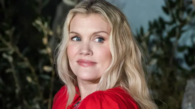 
Emerald Fennell olha por cima do ombro na estreia de *Wuthering Heights* em Londres; ela tem longos cabelos loiros.
