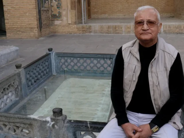 رهنورد زریاب در آرامگاه بایزید بسطامی نشسته و مقبره او در پشت سرش دیده می‌شود