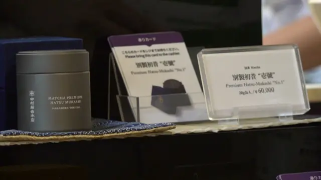 棚に置かれた灰色の抹茶の缶に白字で「MATCHA PREMIUM HATSU MUKASHI」と印刷されている。その隣には「別製初昔　"壱號"　20g缶入／¥60,000」と書かれた値札が並ぶ