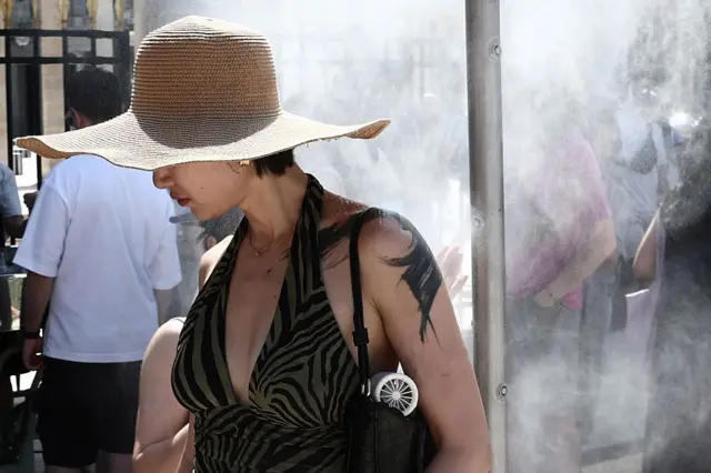 Paris Belediyesi tarafından kurulan bir su püskürtme sisteminin altında yürüyen bir kadın, 21 Haziran 2026'da Paris'te düzenlenen Fransa'nın ulusal müzik festivali Fête de la Musique sırasında sıcak hava dalgasından korunmaya çalışıyor