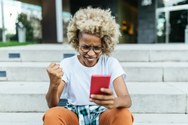 Mulher comemorando olhando para o celular sentadabetano de apostadegraubetano de apostaescada