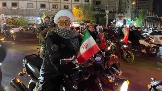 Вооруженные мужчины на мотоциклах, размахивающие иранскими флагами, в центре Тегерана.
