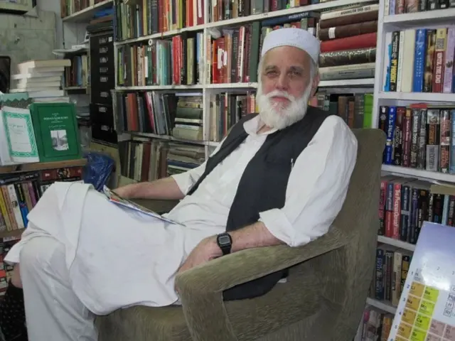 تصویری از پاول ادوین اوربی جونیور با لباس محلی افغانی در یک اتاق با قفسههایی پر از کتاب