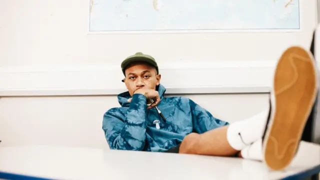 Ben Hurst, um homem negro, de casaco e com as pernas estendidas em uma mesa