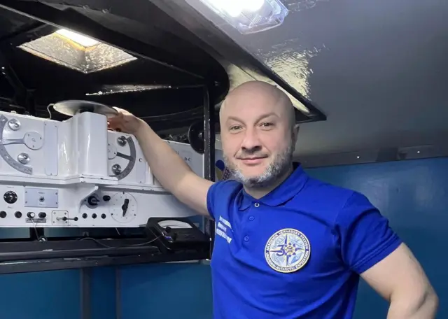 Олександр Полудень у синій футболці стоїть біля спектрофотометра Добсона - білого апарата