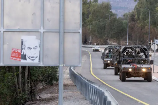 Des véhicules de l'armée israélienne passent devant un panneau de protestation montrant une photo du Premier ministre israélien Benjamin Netanyahu alors qu'ils se déplacent le long de la frontière nord le 20 novembre 2024 dans le nord d'Israël.