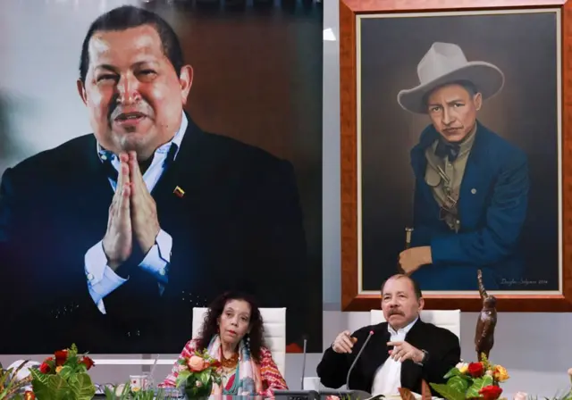 Esta fotografía publicada por la Presidencia de Nicaragua muestra al presidente de Nicaragua, Daniel Ortega (derecha), hablando junto a su esposa y vicepresidenta, Rosario Murillo y frente a una fotografía gigante del fallecido presidente venezolano Hugo Chávez (derecha) durante el XI ALBA. -Cumbre Extraordinaria del TCP (virtual) en Managua el 26 de agosto de 2024. (Foto de César PEREZ/Presidencia de Nicaragua/AFP)