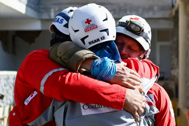 2 Temmuz 2026’da Venezuela’nın La Guaira kentinde, 24 Haziran’daki depremlerin ardından bir haftadan uzun süre enkaz altında kalan sağ kurtulan Hernan Alberto Gil’i çöken bir alışveriş merkezinden çıkarmalarının ardından kurtarma görevlileri birbirlerine sarılıyor.