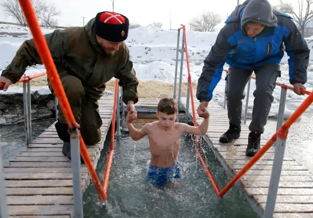 дечак се купа у леденој води у част богојављања у киргистану