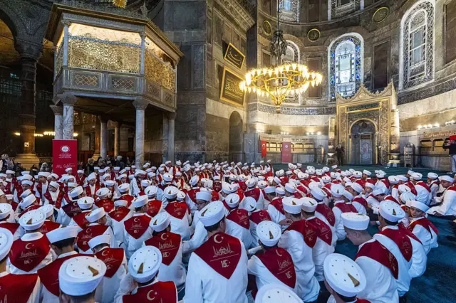 10 Temmuz 2026 tarihinde, 15 Temmuz 2016 darbe girişimi sırasında hayatını kaybedenleri anmak üzere Ayasofya Camii'nde 253 hafızın katılımıyla yapılan Kuran okuma programından bir görüntü. Hafızlar yere oturmuş, üzerilerinde beyaz entariler ve başlarında sarıklar var.