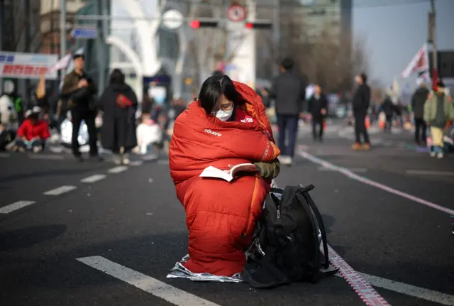 A woman who stayed the night on the street reads a book while waiting for the Constitutional Court ruling on President Yoon Suk Yeol's impeachment, near the Constitutional Court in Seoul, South Korea, April 4, 2025. REUTERS/Kim Hong-ji TPX IMAGES OF THE DAY