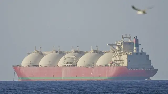 ناقلة نفط حمراء عملاقة ذات خمس قباب بيضاء ضخمة تبتعد عن الكاميرا.