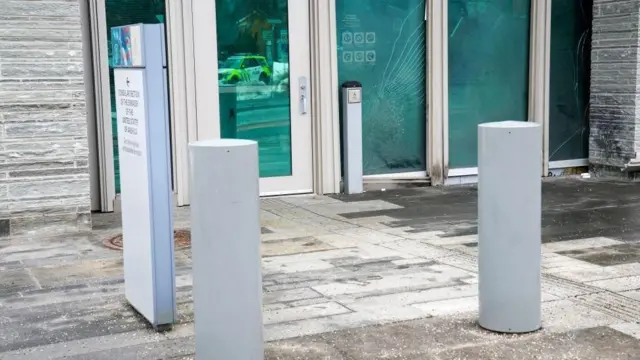 建物のガラスドアの前に白っぽいタイルが敷かれている。ドア付近は黒くなっている。ドアのガラスにはひびが入っている。