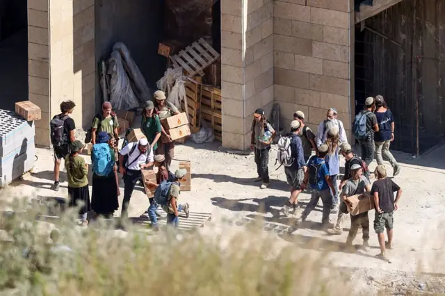 Bir grup İsrailli yerleşimcinin bir şantiyeden yapı malzemeleri alıp taşıdığı görülüyor.