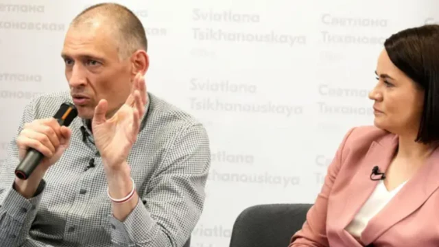 Сергей Тихановский с микрофоном в руках в рубашке в мелкую клетку, рядом с ним его жена Светлана в пиджаке кораллового цвета. Это первая пресс-конференция Тихановского после освобождения в июне 2025 года