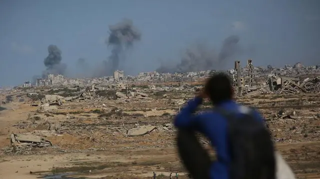 Una persona sentada en un montículo observa las columnas de humo en la distancia de los ataques israelíes en Ciudad de Gaza. 