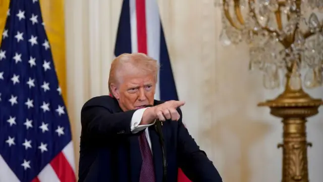 Trump aponta para a audiência, em frente a bandeiras dos Estados Unidos e do Reino Unido