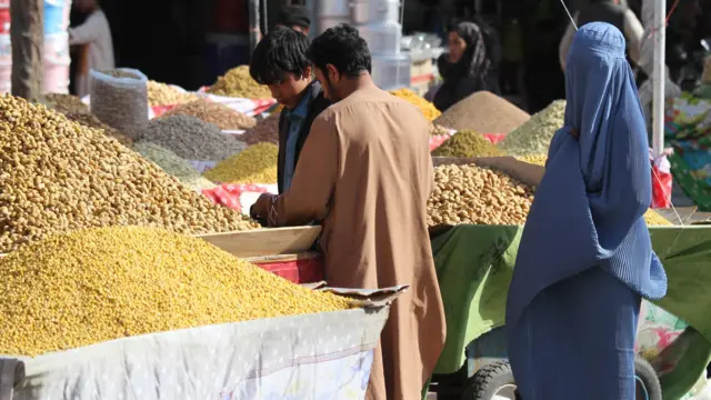 تصویر یک زن در کنار غرفه میوه خشک در هرات . زن برقع با چادری پوشیده است