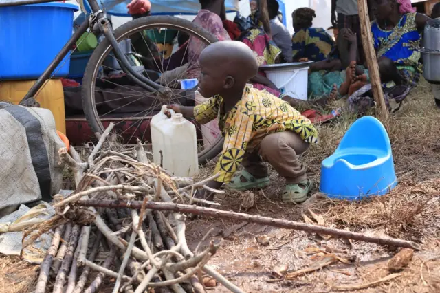 Umugore w'impuzi ariko aratora umuceri akikujwe n'abana ku kibuga c'umupira ca Rugombo aho yahungiye