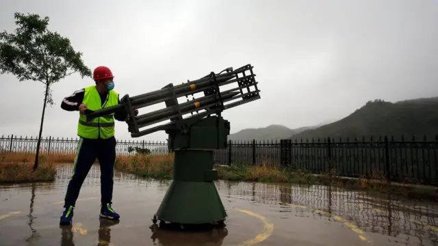 चीन के हेबेई प्रांत के शीज़ीयाज़ूआंग के स्थानीय मौसम विज्ञान ब्यूरो का एक कर्मचारी 15 मई, 2021 को बारिश कराने के प्रयास में क्लाउड-सीडिंग रॉकेट दागता हुआ. 