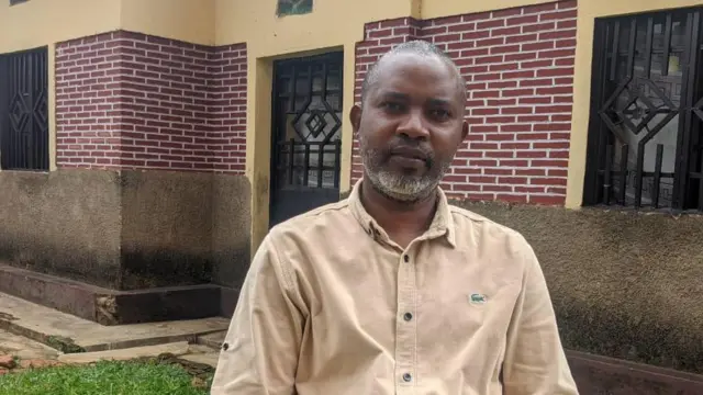 Umugabo wicaye imbere y'inzu, yambaye ishati y'amaboko maremare y'ibara rya khaki