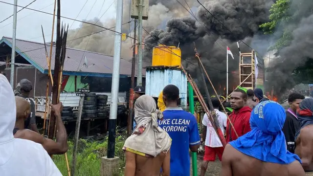Massa berdiri di depan pos Satgas 123/Rajawali yang terbakar. Mereka menagih pertanggungjawaban TNI atas kematian Erenius.