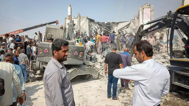 Жители Минаба разбирают завалы у разрушенной школы - видна строительная техника и руины здания