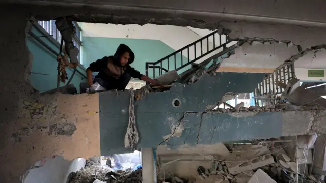 
L'intérieur d'un bâtiment, des murs endommagés et des décombres. Un adolescent regarde les dégâts.