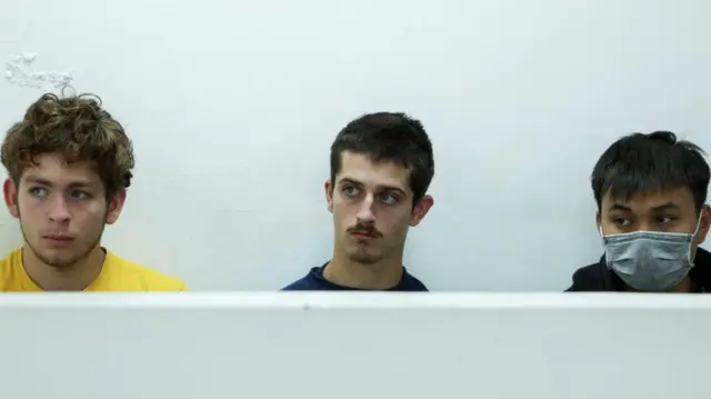 Les ressortissants belges David Lornoy, portant un T-shirt jaune, et Seppe Lodewijckx, portant un T-shirt noir, sont assis à côté du ressortissant vietnamien Duh Hung Nyugen, qui porte un masque de protection. 