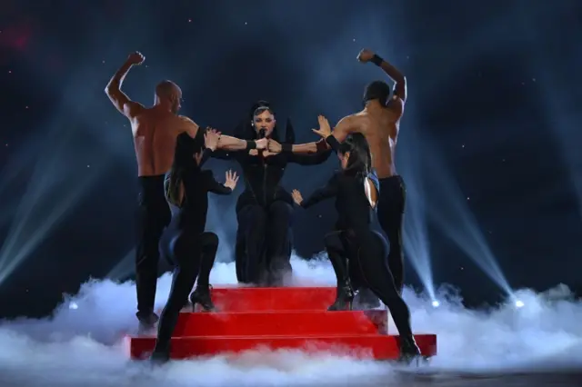 Певачица на црвеним степеницама, окружена плесачима и плесачицама