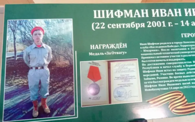 На зеленому тлі - поверхня "парти героя", де ліворуч - фото юнака в бежевій уніформі та береті "Юнармії". Посередині - посвідчення про вручення медалі. Праворуч - біографія, "прикрашена" забороненою в Україні георгіївською стрічкою.