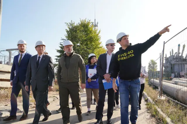 Японська делегація на чолі з Кудрицьким у білих робочих касках на тлі енергообʼєкту