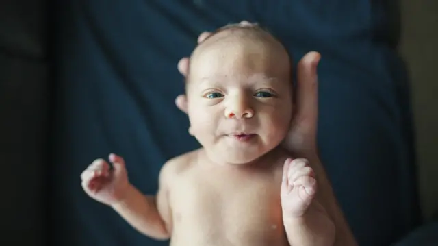 Bebê pequeno temestrelabet apostacabeça segurada por mão humana e olha diretamente para a câmera