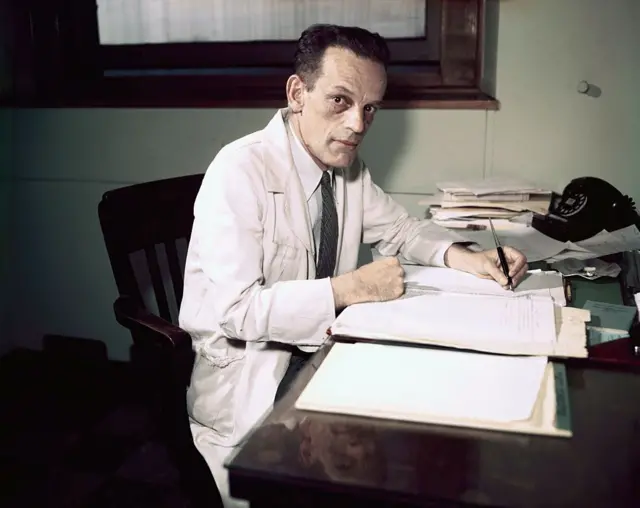 Le Dr Max Theiler de la Fondation Rockefeller assis sur un bureau. (Photo 17 octobre 1951).
