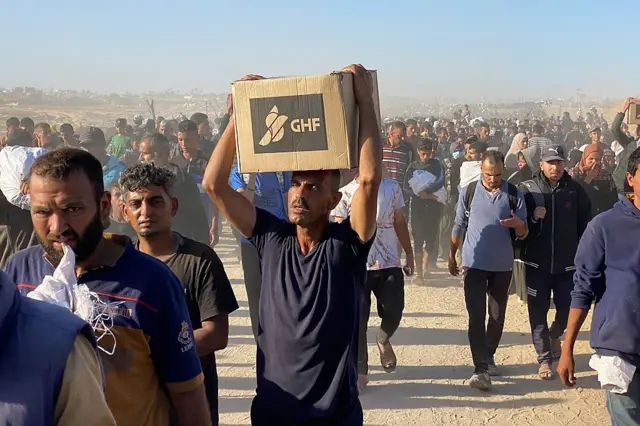 Personas llevan cajas de ayuda de la GHF.