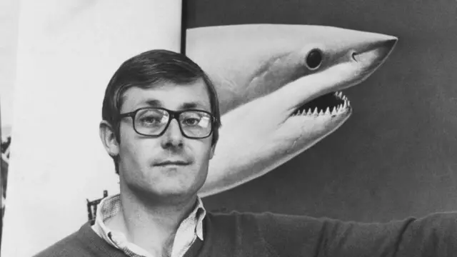 Peter Benchley, autor do livro que deu origem ao filme 'Tubarão', em frente a uma foto do animal.