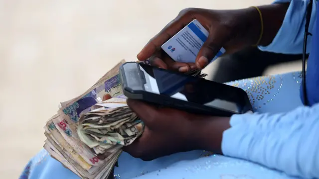 Person holding bundles of naira in cash and a mobile phone