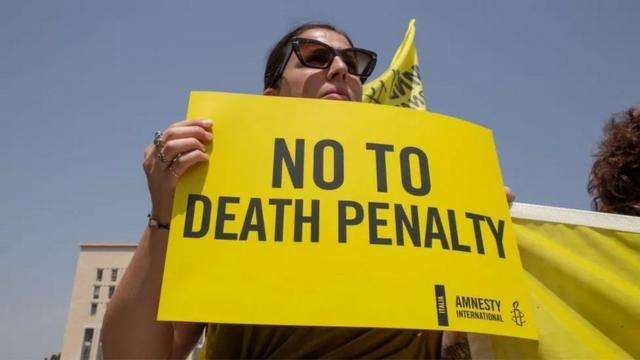 Mulher segura cartaz em inglês que pede fim das execuções