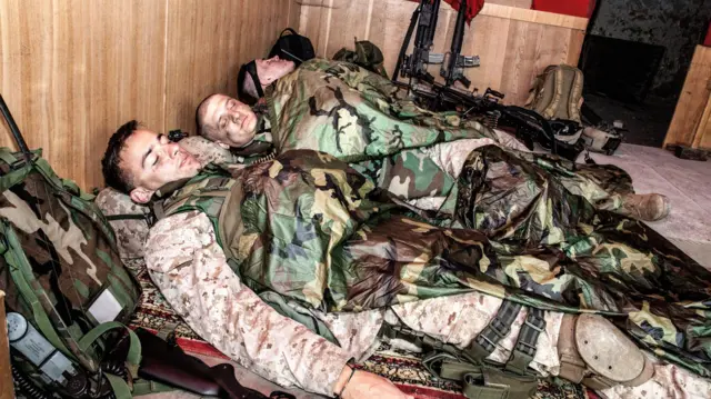 Тројица војника, обучени у камуфлажне унироме и са панцирима, спавају у углу собе. Наслоњени су на ранчеве, а оружје им је надохват руке, као да ц́е сваког тренутка бити спремни да се врате на прву линију фронта.