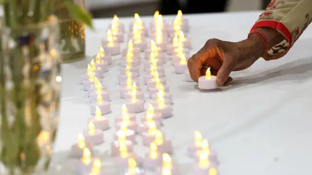 Uma mulher acende uma vela ao lado de fileiras de outras velas