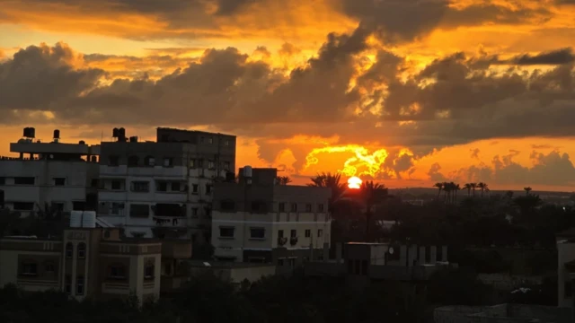 طلوع آفتاب از بالکنی یک خانه. خانه‌های شهر از میان نور نارنجی و آسمانی با چند ابر دیده می‌شوند