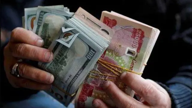 شخص يحمل بين كفيه دنانير عراقية ودولارات أمريكية.
