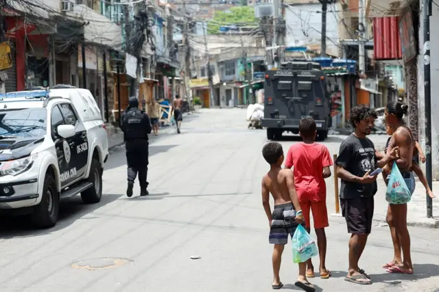 Imagem de moradores de comunidade do Rio com veículos da polícia ao fundo durante operação do dia 28 de outubro de 2025