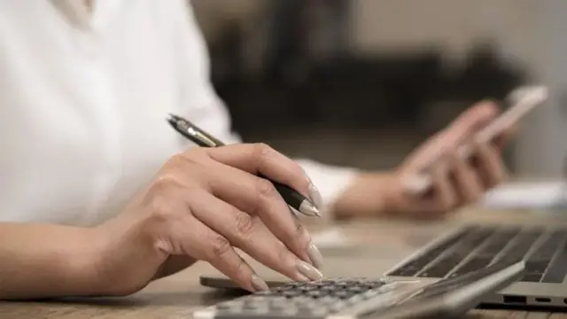 Uma mão usando uma calculadora em uma mesa