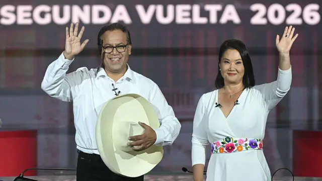 Roberto Sánchez, con una camisa blanca y un sombrero, y Keiko Fujimori, quien lleva puesto un vestido blanco con flores pintadas alrededor de la cintura. Ambos saludan a las cámaras.