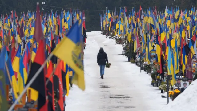 Uma pessoa caminha por um memorial, com flores nas mãos, em Lviv