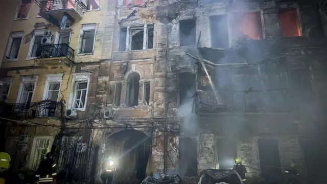 Фасад старого здания со следами пожара, в окнах видно пламя